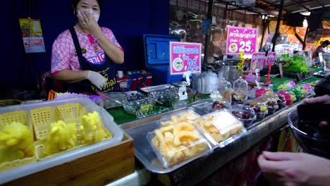 Comida-Y-Frutas-Exhibidas-Con-Una-Dama-Vendedora-En-El-Mercado-Al-Aire-Libre-De-Tailandia