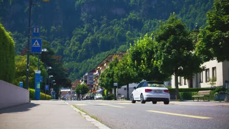 Elderly-Man-Rushing-To-Cross-The-Street-As-Car-Passes---Hergiswil-Switzerland-Mountains-in-4K