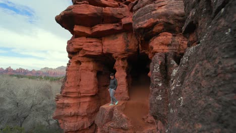 Young-brunette-female-walks-out-of-wind-cave-onto-platform-rock-in-Sedona