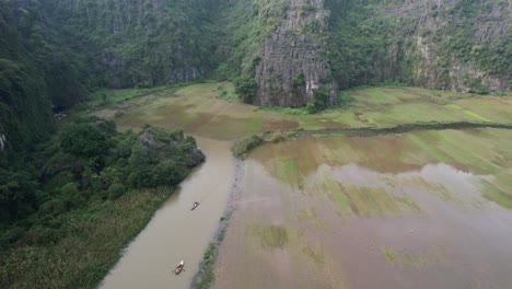 Ngo-Dong-River-Flooded-Agricultural-Rice-Fields-and-People-Travel-on-Sampan-Boats-in-Limestone-Gorge-in-Ninh-Binh-Park,-Vietnam---Drone-Flyover