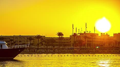 Amanecer-Time-lapse-En-La-Playa-De-Hurghada-Con-Palmeras,-Resorts-Y-Yate-Al-Amanecer-Egipto,-áfrica
