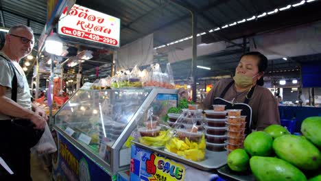Hombre-Caucásico-Comprando-Comida-A-Una-Dama-En-Un-Mercado-Interior-En-Tailandia