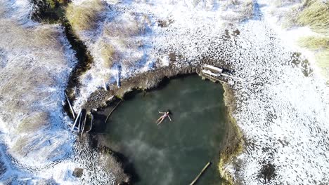 Mujer-Nadadora-Flotando-Panza-Arriba-En-Saratoga-Hot-Springs-En-Provo-Utah-Durante-El-Invierno-Con-Nieve-Por-Todo-El-Suelo-Antena-De-Arriba-Hacia-Abajo
