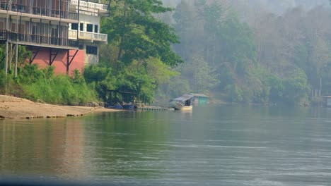 Kleineres-Gelbes-Boot,-Das-Auf-Dem-Fluss-Fährt,-Mit-Naturkulisse-Und-Einem-Hotel-Im-Hintergrund