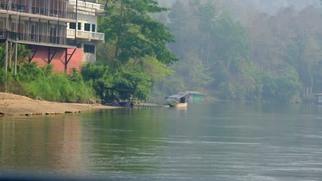 Barco-Amarillo-Más-Pequeño-Navegando-Por-El-Río-Con-Escenarios-Naturales-Y-Un-Hotel-En-El-Fondo