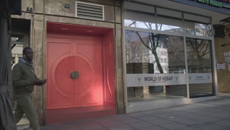 Black-Man-Walking-Near-Bright-Red-Shop-Door-On-Street--Schlossplatz-In-Downtown-Stuttgart-in-4K,-Classic-Germany-Architecture,-Famous,-Red-Komodo-Cooke-Mini-S4i-Lens-Premium-Quality-|-News