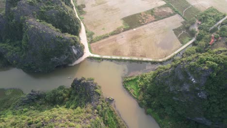 Flying-Above-Summits-And-Steep-Slopes-of-Limestone-Mountain-Ranges,-Tilt-Down-on-Ngo-Dong-River-in-Ninh-Binh-Vietnam-at-Sunset