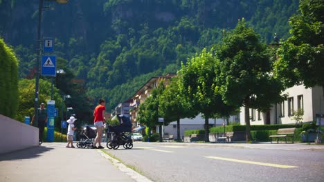 Car-Passing-As-Mother,-Daughter,-and-Baby-Cross-Street---Hergiswil-Switzerland-Mountains-in-4K