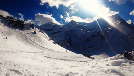 timelapse-in-the-ski-slope-with-moving-clouds,-the-sun,-snowy-mountains-and-skiers