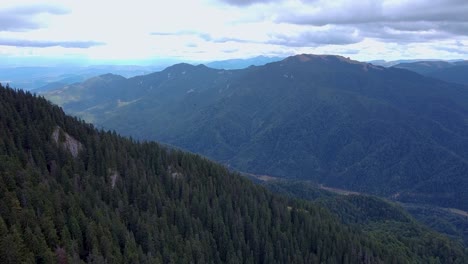 Eine-Atemberaubende-Luftaufnahme-Eines-üppig-Grünen-Bergwaldes-Mit-Hohen-Gipfeln-Im-Hintergrund,-Umgeben-Von-Flauschigen-Weißen-Wolken,-Im-Wunderschönen-Poiana-Brasov,-Rumänien