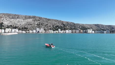 Antena-Pan-Pescadores-Entrando-En-El-Puerto-Con-La-Ciudad-Costera-De-Montaña-Detrás