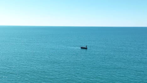 Aerial-static-shot-of-lone-man-standing-on-small-boat-in-open-seas