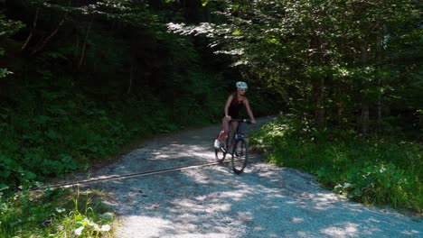 Woman-rides-her-mountain-bike-down-a-gravel-mountain-road-on-a-sunny-summer-day