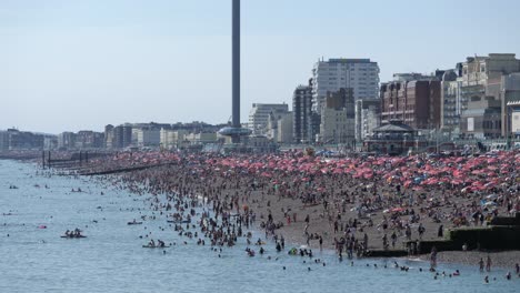 Brighton-beach-in-heatwave-crowded-with-people-relaxing-in-the-hot-sun,-cooling-off-in-the-sea-with-i360-in-background