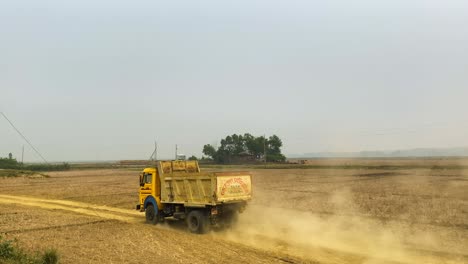yellow-construction-truck-drives-down-dry-dirt-road-in-farmland-field