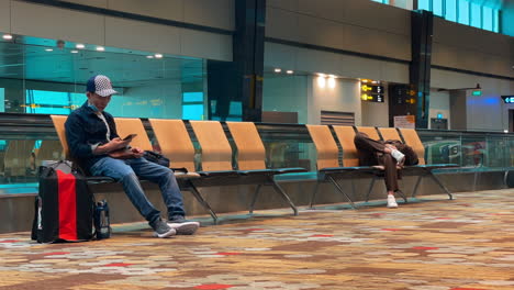 Gelangweilte-Asiatische-Und-Punjabi-Männer,-Die-Mobiltelefone-Benutzen,-Während-Sie-Am-Flughafen-Auf-Ihren-Flug-Warten