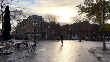 Slow-motion-shot-of-woman-on-bicycle-riding-on-street-in-city-of-leiden-during-sunset,Netherlands---Static-wide-shot