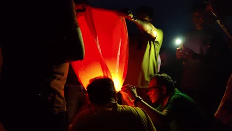 Asiático,-Joven-Enciende-Una-Linterna-De-Cielo-Naranja,-Fanush-En-La-Noche-Oscura