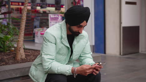 Indischer-Sikh-Mann-Mit-Schwarzem-Turban-Nutzt-Smartphone-Im-Freien
