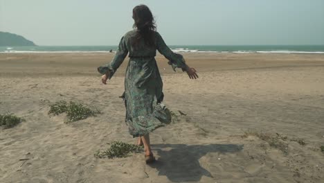 Young-woman-walking-on-beach,-windy-breeze-plays-with-her-dress,-freedom-feeling