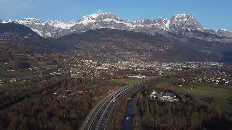 Sallanches,-France-in-a-valley-below-the-rugged,-snow-capped-Alps---aerial-flyover
