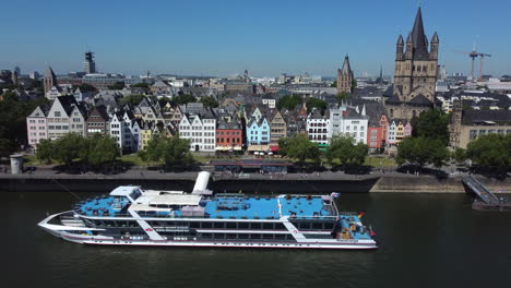 Drone-shot-of-old-town-Cologne-right-at-Rhine-river---drone-is-facing-a-boat-in-front-of-ancient-houses