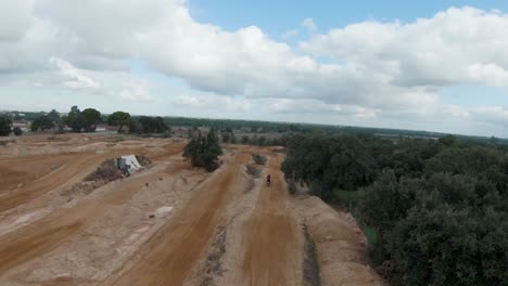 Panoramic-aerial-view-of-motocross-rider-taking-jumps-on-straightaway
