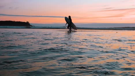 A-surfer-leaving-the-water-at-sunset-in-Tofino,-British-Columbia