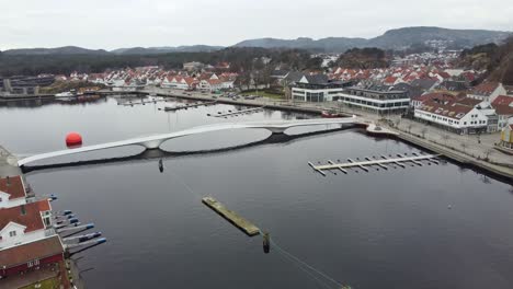 Unique-Adolph-Tidemands-bridge-crossing-Marna-river-in-Mandal-Norway---Aerial-approaching-and-flying-over-bridge-for-pedestrians-and-bicycles-in-city-center