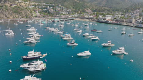 Flying-Above-Boats-Sitting-in-Harbor-on-Beautiful-Clear-Day,-Catalina-Island-Drone-Shot-of-Avalon-City-in-California