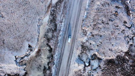Aerial-top-down-shot-of-van-driving-on-snowy-road-in-icelandic-landscape-near-Mount-Búlandstindur