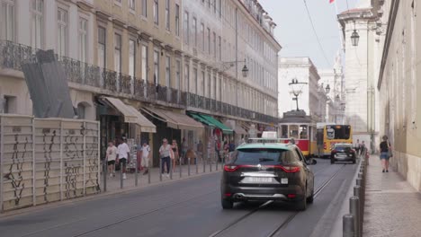 Tram-streetcar-passes-down-historic-Lisbon-road-street-with-taxis,-bus-and-person-on-a-scooter-driving-past,-Portugal,-Europe
