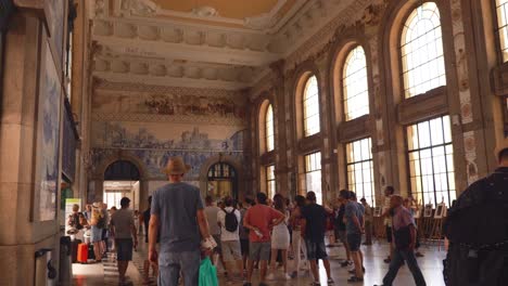 Wide-angle-shot-of-people-in-entrance-hall-of-Sao-Bento-Railway-Station,-architectural-landmark-in-Historic-Centre-of-Porto,-Portugal,-blue-tile-mural-on-wall-2022