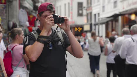 Hipster-tourist-in-black-Adidas-shirt-and-baseball-cap-taking-photo-with-dslr-camera-in-the-city-street---Brussels,-Belgium