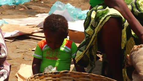 Boy-eats-a-snack-sitting-by-his-mother-as-she-sells-goods-at-the-market