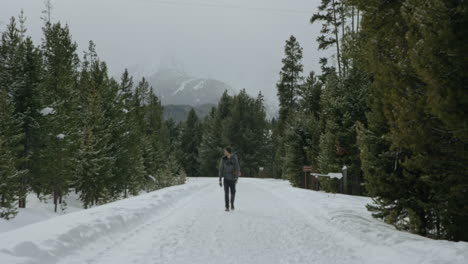 Man-walking-on-snow-covered-road-in-forest-during-winter-with-backpack