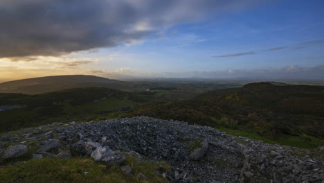 Timelapse-of-rural-nature-landscape-with-ruins-of-prehistoric-passage-tomb-stone-blocks-in-the-foreground-during-sunny-cloudy-evening-viewed-from-Carrowkeel-in-county-Sligo-in-Ireland