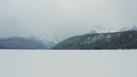 Aerial-over-frozen-Redfish-Lake-with-Sawtooth-Mountains-in-fog-behind