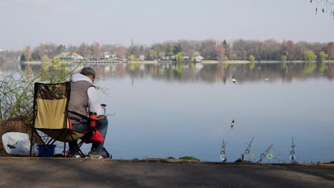 Man-Sits-And-Watches-His-Fishing-Rods-In-The-Lake-Water-On-A-Sunny-Morning