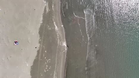 Aerial-pan-of-shoreline-with-gentle-windswept-waves-crashing-on-beach