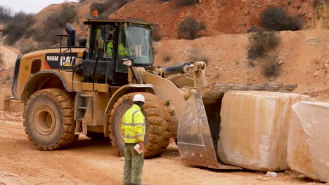 Loader-excavator-vehicle-depositing-big-limestone-block-in-a-row,-Medium-shot