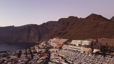 Vacation-resort-buildings-surrounded-by-towering-massive-cliffs-Los-Gigantes,-Tenerife