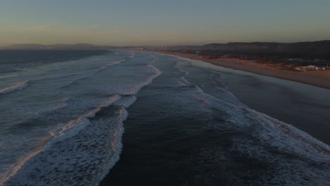 Drone-shot-of-Costa-Caparica-beach-near-Lisbon-during-sunset---drone-is-flying-backwards-over-the-water