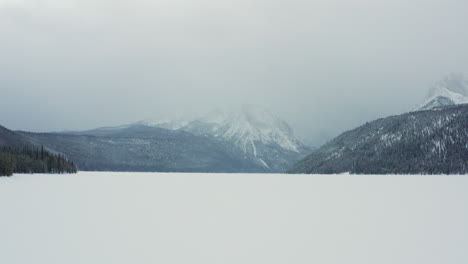 Luftaufnahmen,-Die-Sich-Im-Winter-Tief-über-Dem-Zugefrorenen-See-Bewegen,-Mit-Aufragenden-Bergen-Dahinter