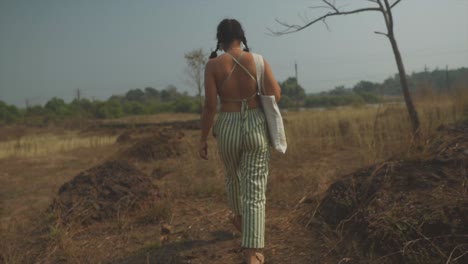 A-woman-dressed-in-green-and-white-walks-in-slow-motion-through-sunlit-fields,-viewed-from-behind---a-serene-and-picturesque-moment-on-a-sunny-day