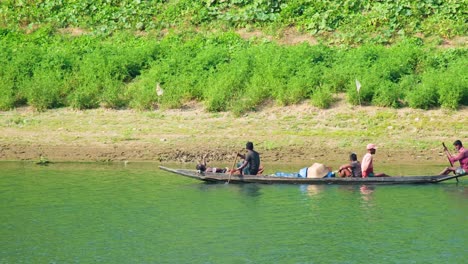 Fishermen-paddling-canoe-on-water-by-shore-in-Sylhet,-Bangladesh