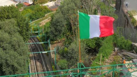Italian-flag-blowing-in-the-wind-overlooking-railroad-in-Capri,-Italy
