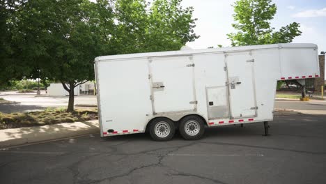 Small-white-gooseneck-cargo-trailer-in-an-empty-parking-lot,-pan