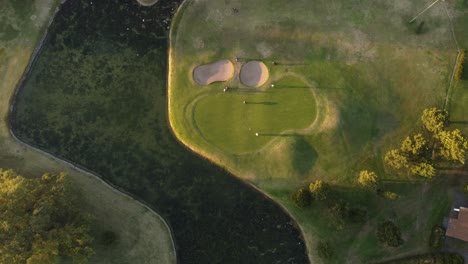 Golfers-on-golf-course-green-at-sunset,-top-down-aerial-view