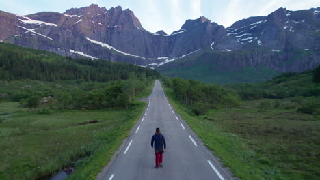 Aerial-backwards-shot-of-a-tourist-walking-on-the-scenic-road-to-Nusfjord-in-Lofoten,-called-Batman-Wall